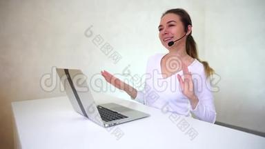 年轻的金发女人，扎着马尾辫，坐在桌子旁边，在光线充足的房间里拿着银色的笔记本电脑，接电话。